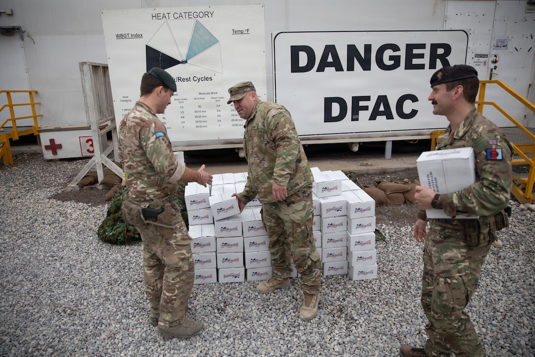 U.S. Army Sgt. Maj. Chad Fischer, operations sergeant major for 2nd Brigade Combat Team, 34th Infantry Division, Iowa National Guard, gives packages from Operation Gratitude to two coalition soldiers in front of Logistics Support Area Danger’s dining facility located in Erbil Air Base, Iraq, Dec. 14, 2025. Operation Gratitude honors service members with year-round appreciation, meaningful engagement opportunities, and care packages that recognize their service and sacrifice. (U.S. Army Photo by Pfc. Jordan Foster)