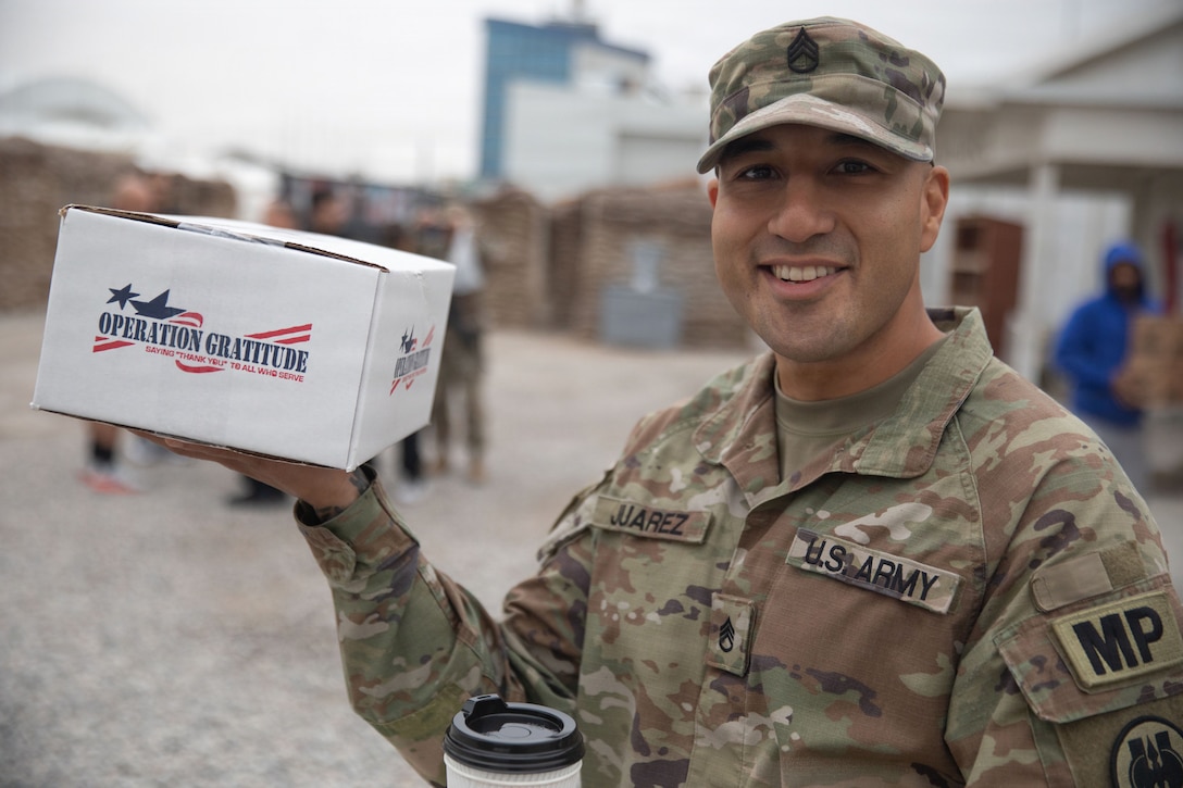 U.S. Army Staff Sgt. Ernesto Juarez, the military police investigation noncommissioned officer in charge, holds up a care package from Operation Gratitude inside Erbil Air Base, Iraq, Dec. 14, 2025. Operation Gratitude honors service members with year-round appreciation, meaningful engagement opportunities, and care packages that recognize their service and sacrifice. (U.S. Army Photo by Pfc. Jordan Foster)