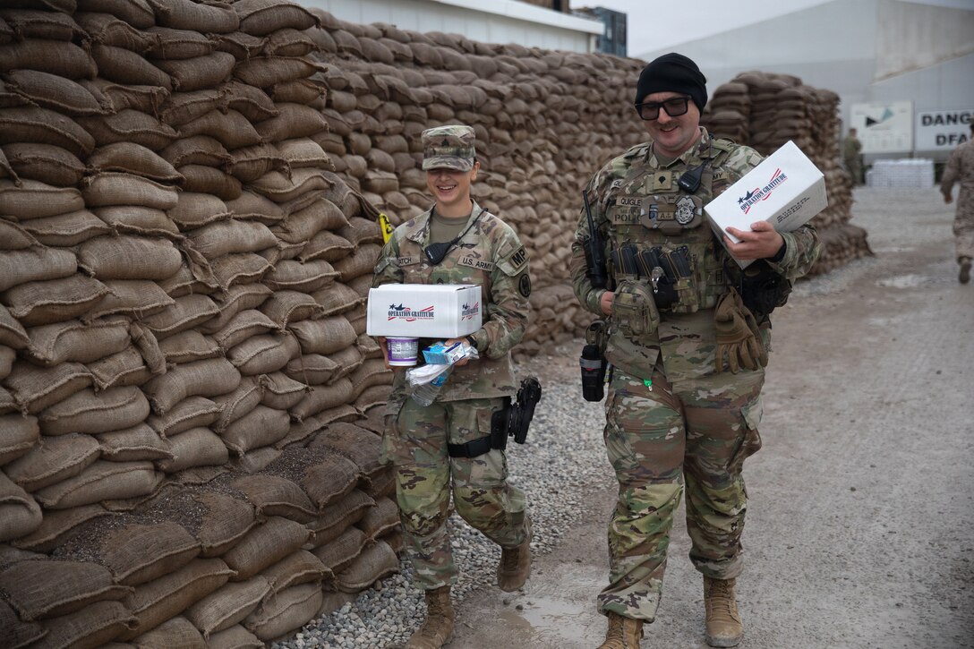 Two U.S. Army soldiers walk away from Logistics Support Area Danger’s dining facility with Operation Gratitude care packages in their hands in Erbil Air Base, Iraq, Dec. 14, 2025. Operation Gratitude supports U.S. service members with gratitude-filled care packages in effort to uplift spirits. (U.S. Army Photo by Pfc. Jordan Foster)