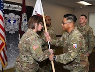 Capt. Justine Juan, right, commander of U.S. Army Medical Logistics Command’s Headquarters and Headquarters Detachment, passes the unit guidon to incoming detachment sergeant, Sgt. 1st Class Brandi Brown, during a change of responsibility ceremony Dec. 12, 2025, at Fort Detrick, Md. Also pictured are Sgt. 1st Class Aaron Taylor, background center, and outgoing detachment sergeant, Master Sgt. William Harbeson.