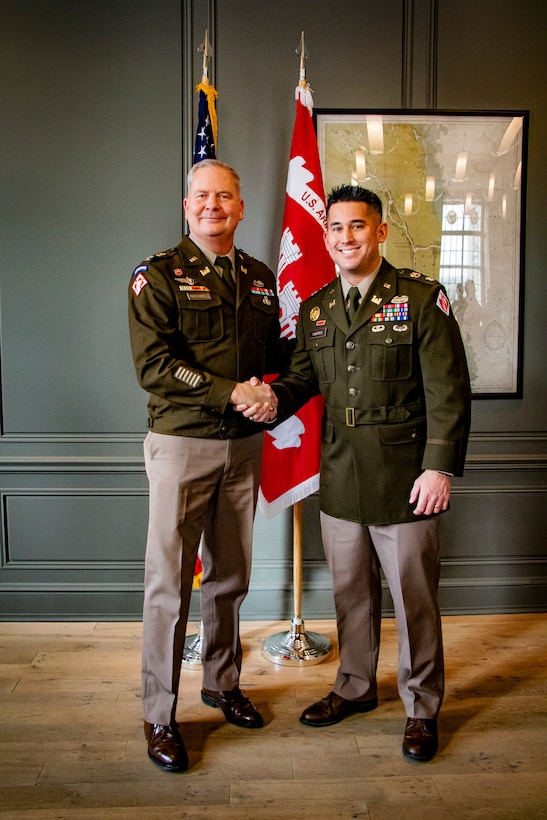 COL Rockwell and LTC Harpen dressed in Army Class A uniforms shake hands in from of the U.S. Army Engineer flag.