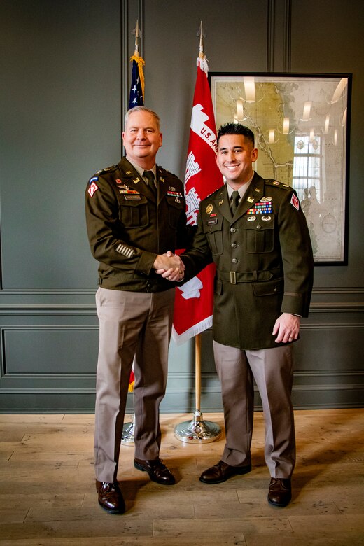COL Rockwell and LTC Harpen dressed in Army Class A uniforms shake hands in from of the U.S. Army Engineer flag.