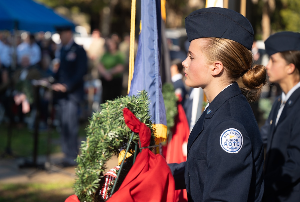 n Air Force Junior ROTC member stands in front of a wreath during the Wreaths Across America Placement Ceremony.
