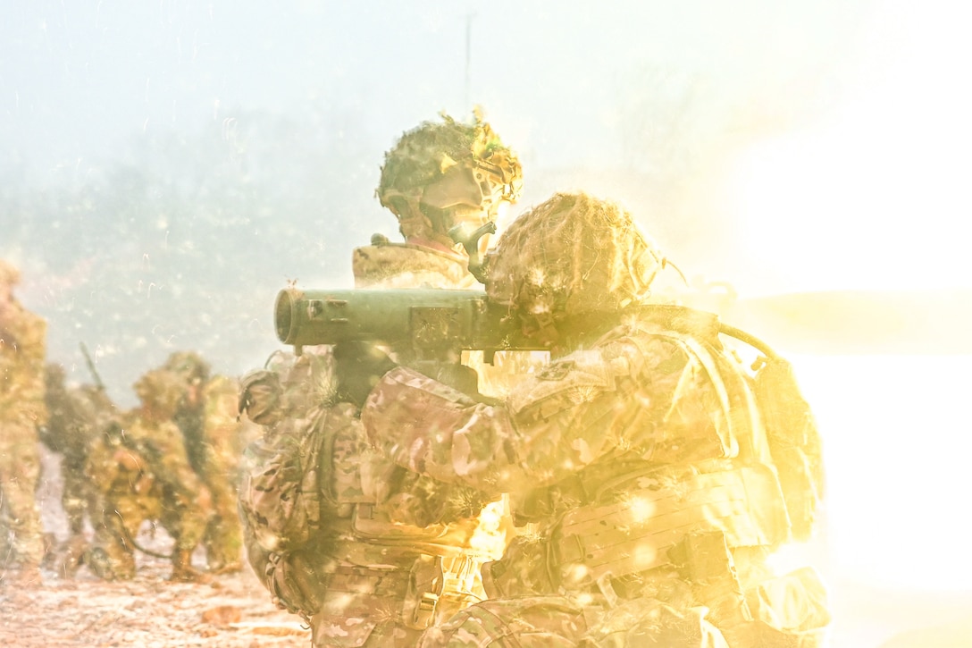 A soldier fires a weapon next to a fellow soldier, creating a bright, hazy fireball.