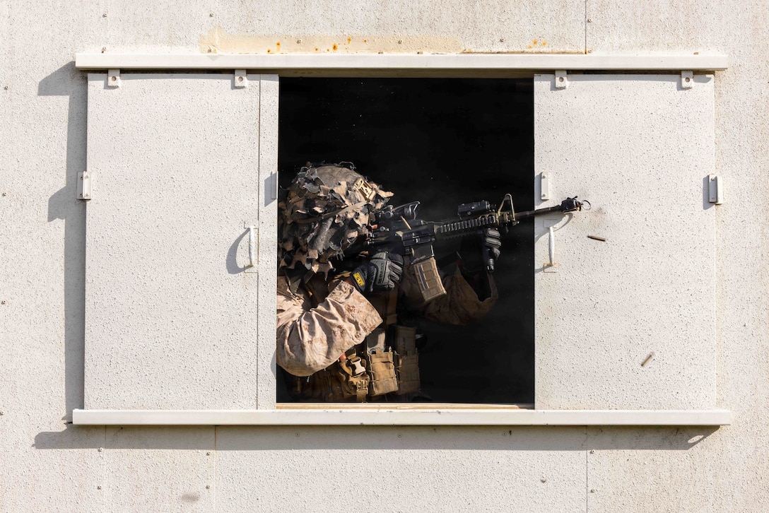 Ammo falls as a Marine in tactical gear fires a weapon out of a window.