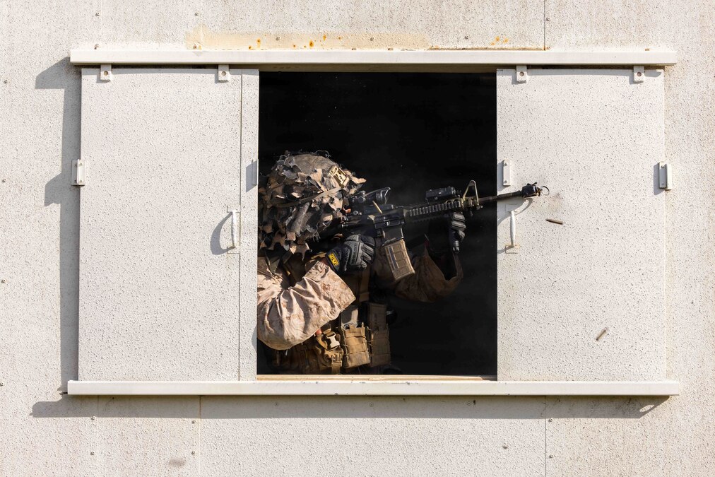 Ammo falls as a Marine in tactical gear fires a weapon out of a window.