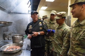 Celebrity chef Marc Cummings, left, demonstrates cooking techniques to 436th Force Support Squadron food service Airmen at the Patterson Dining Facility on Dover Air Force Base, Delaware, Dec. 10, 2025. Chef Cummings spent three days at the dining facility sharing his knowledge and tips with the Airmen while preparing and cooking a specific lunchtime entrée for each day. (U.S. Air Force photo by Roland Balik)