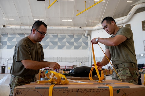 From left, U.S. Air Force Senior Airman Madison Sinclair, 374th Air Expeditionary Wing combat mobility flight combat mobility technician, and Lt. Col. Jae Kim, 374th Logistics Readiness Squadron commander, secure humanitarian aid bundles.