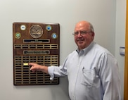 Pittsfield, Mass. - Frank LaRagione, chief engineer at PMOSPS (retired), points to a new entry placeholder on a plaque in Pittsfield, Mass., in Spring 2025. The plaque recognizes members of the PMOSPS technical workforce that have completed the Technical Discipline Training and Qualification Program (TDTQP). TDTQP provides a fundamental understanding of the technical policies, processes, and acquisition management tools that underpin the nation’s Trident II D5 strategic weapons system (SWS), nuclear-armed sea launched cruise missile (SLCM-N), and the non-nuclear hypersonic conventional prompt strike system (CPS).