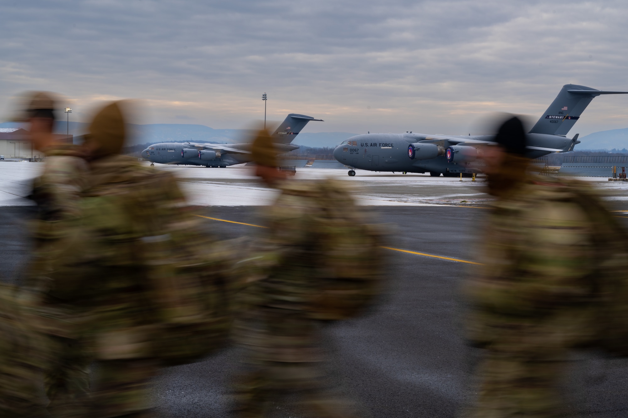 an image of blurry U.S. Airmen march in front of refueling aircraft in the background.