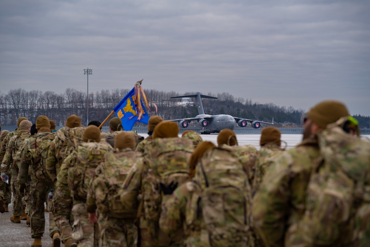U.S. Airmen in winter uniforms march across a grey-skyed flightline with U.S. aircraft in the background.