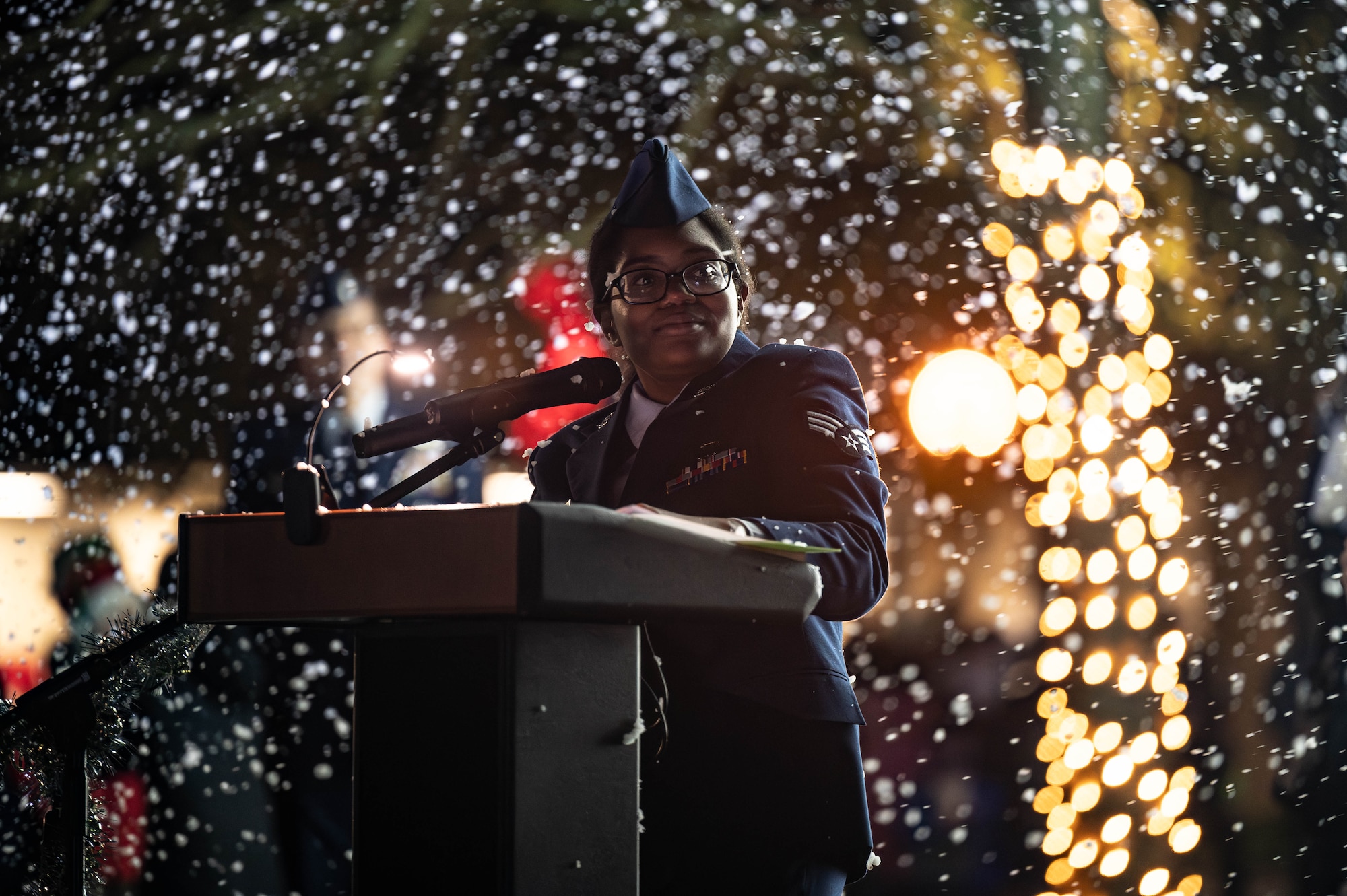an airman speaks at a podium in Air Force service dress as snow falls around her
