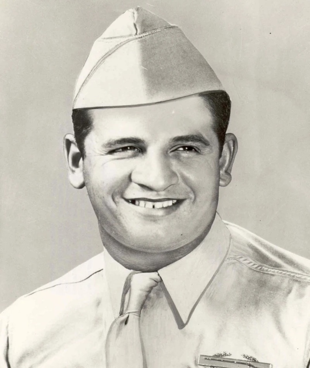 A man in a cap and military dress uniform smiles for a photo.