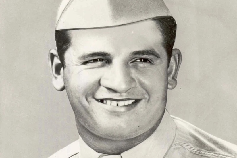 A man in a cap and military dress uniform smiles for a photo.
