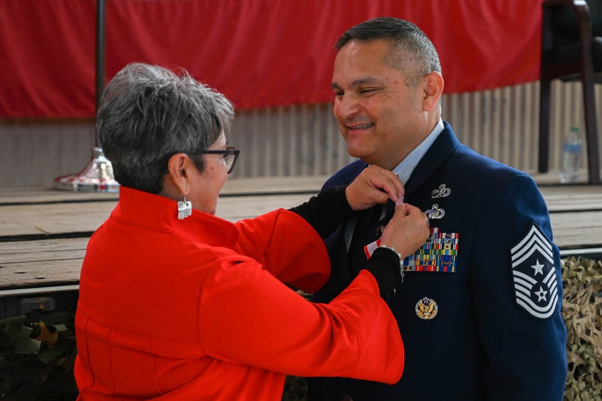 A man in a U.S. Air Force dress uniform attends a ceremony for his retirement. His wife is attaching a retirement pin to his uniform.