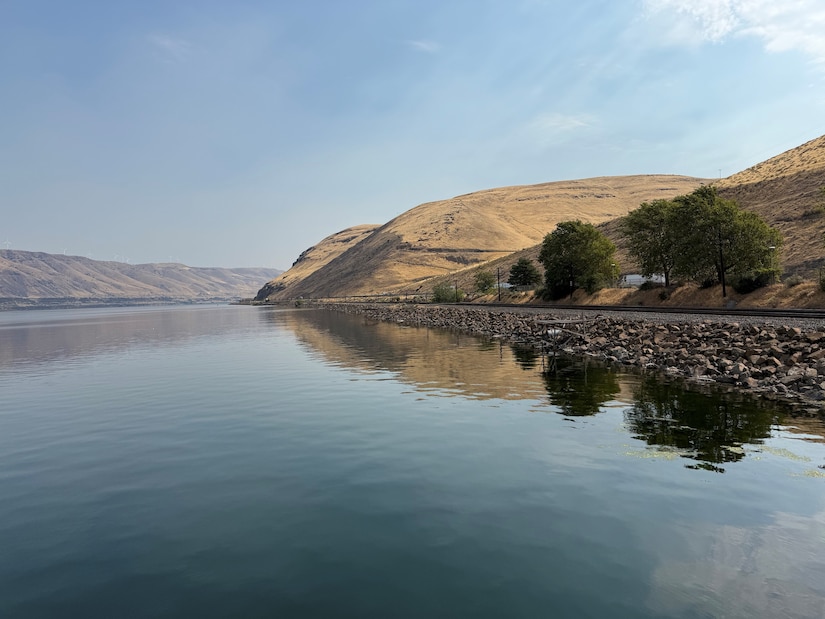 A calm body of water with a rocky shore and brown hilltops on the sides.