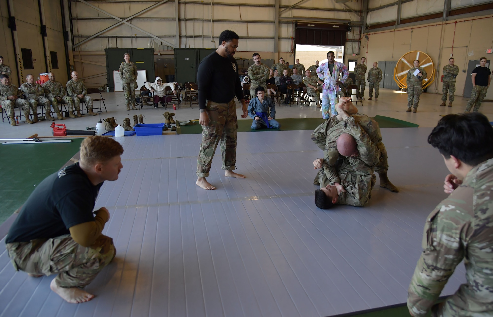 A group of people watch as two men wearing military uniforms wrestle.
