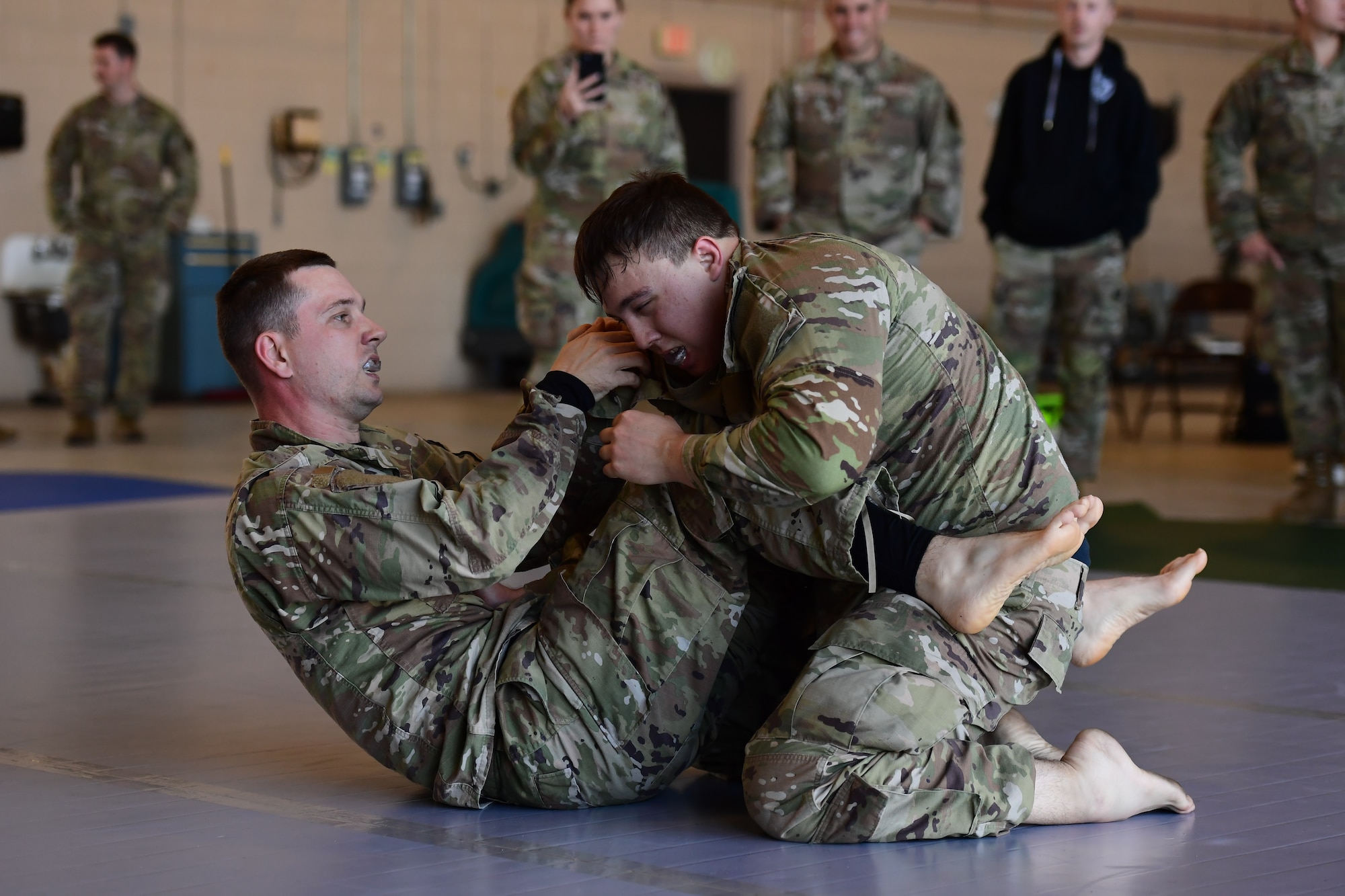 Two men wearing military uniforms wrestle.