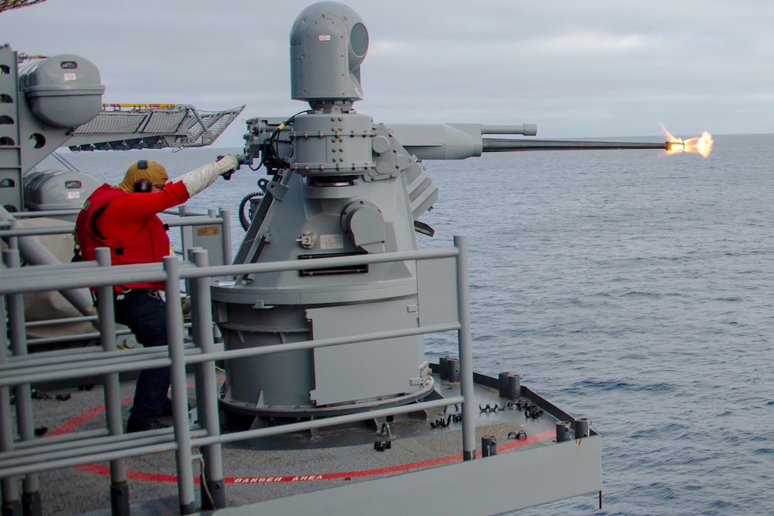 A sailor fires a weapon on a ship, creating a small fireball on a gloomy day.
