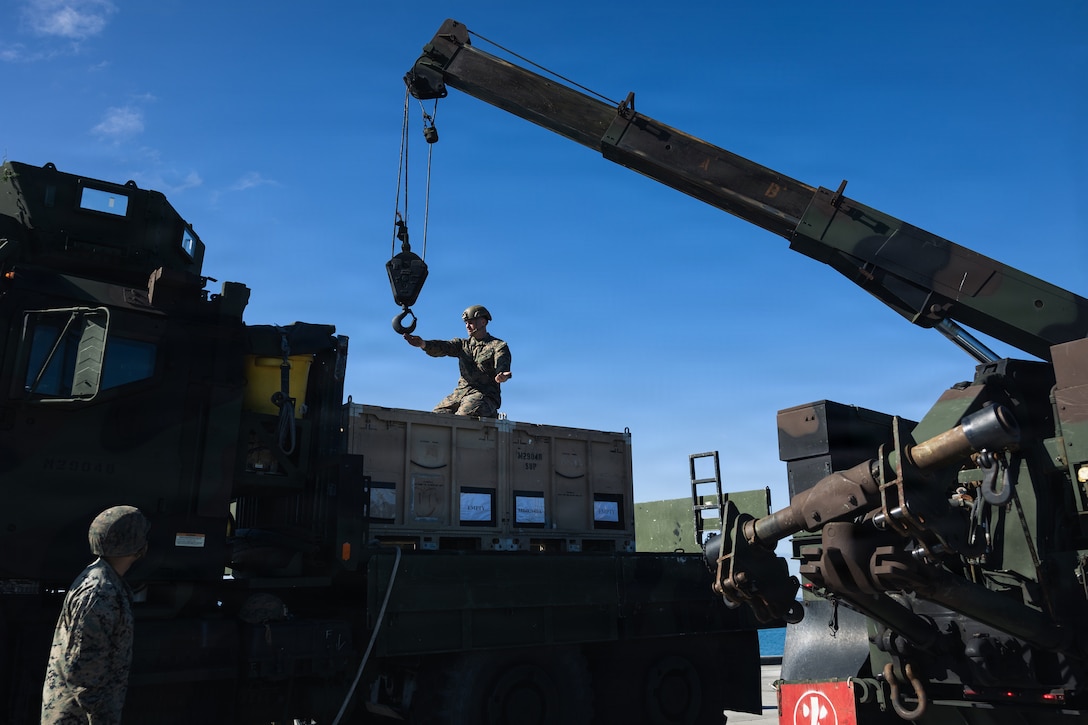 U.S. Marine Corps Sgt. Ryan O’neal, a wrecker operator with Combat Logistics Battalion 31, 31st Marine Expeditionary Unit, guides material handling equipment during unmanned surface vessel training operations as part of MEU Exercise at White Beach Naval Facility, Okinawa, Japan on Dec. 2, 2025. The autonomous low-profile vessel has the ability to deliver multiple variations of supplies and equipment through contested maritime terrain. The 31st MEU, the Marine Corps’ only continuously forward deployed MEU, provides a flexible and lethal force, ready to perform a wide range of military operations as the premiere crisis response force in the Indo-Pacific region. (U.S. Marine Corps photo by Sgt. Alora Finigan)