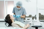 Dentist uses dental equipment on a patient in a white room