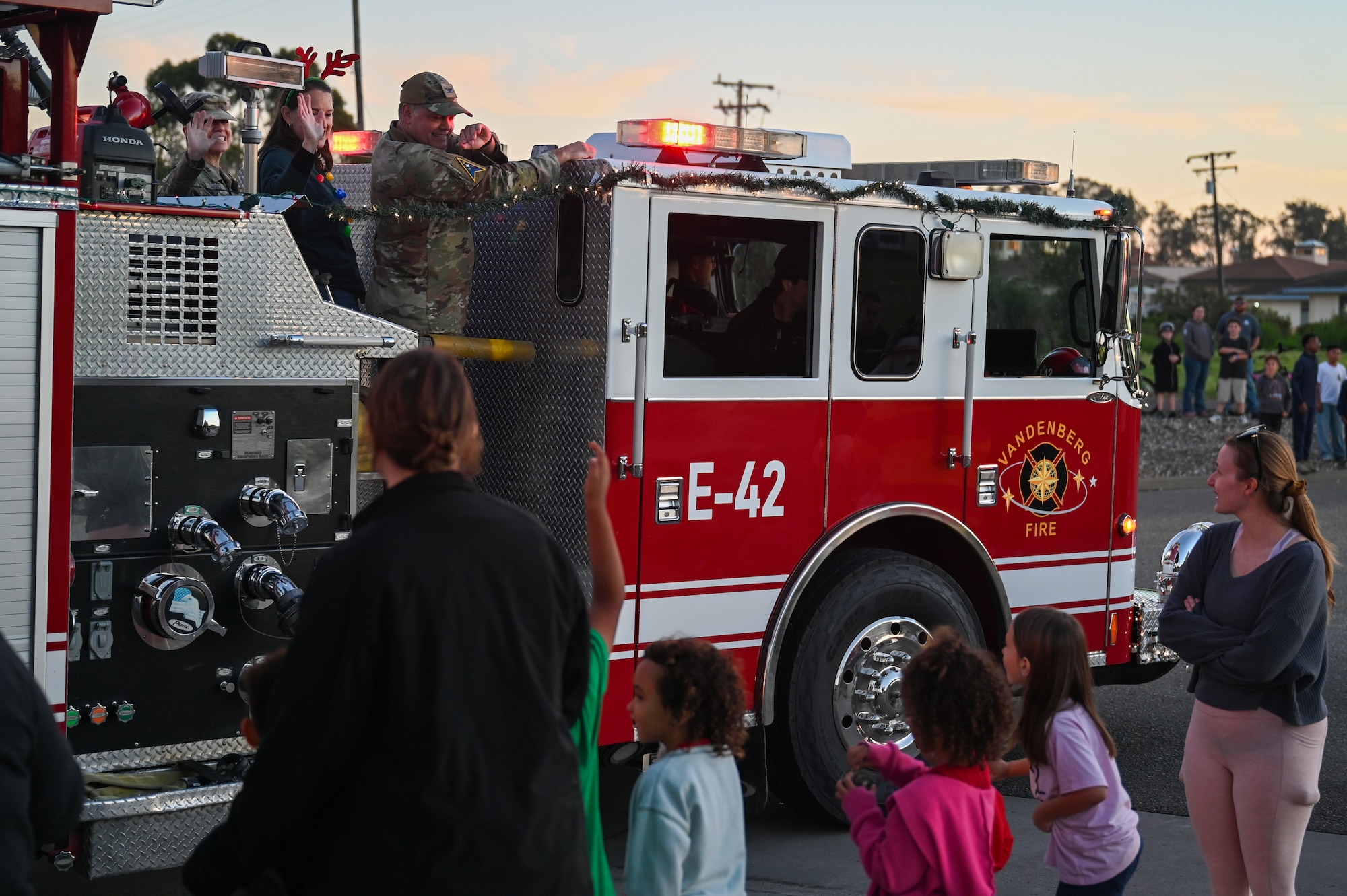U.S. Space Force Col. James T. Horne III, Space Launch Delta 30 commander, and U.S. Space Force Chief Master Sgt. Shannan Sanchez, SLD 30 senior enlisted leader, waves to the crowd during the 2025 Holiday Parade. They are on a firetruck passing by the crowd.