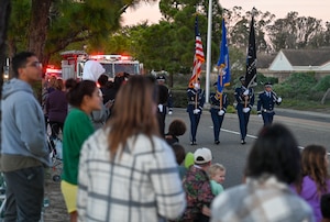 U.S. Air Force Vandenberg Honor Guard leads the 2025 Holiday Parade. They are walking in the middle of the street holding flags.