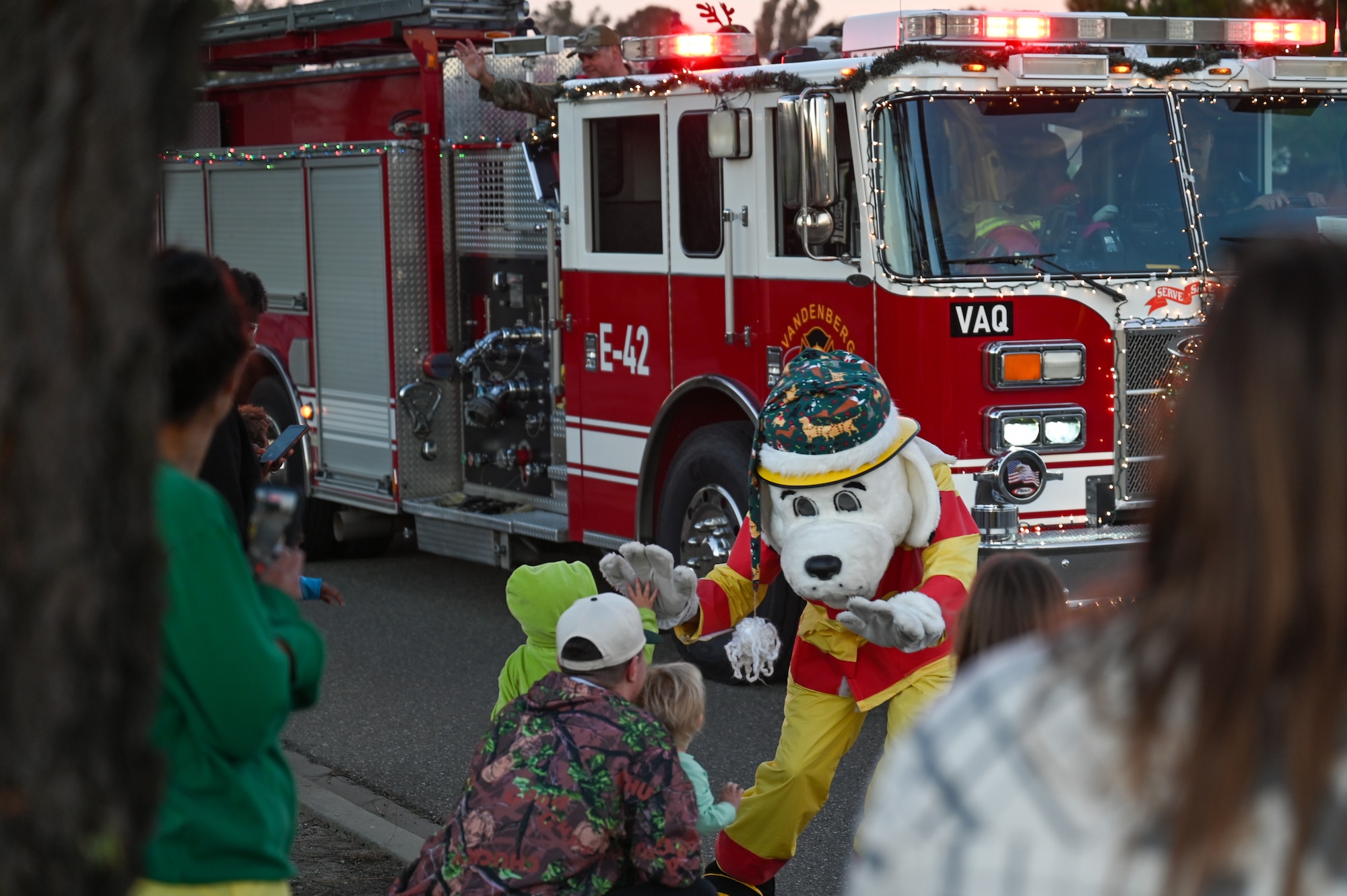 Sparky the Dog, Vandenberg’s fire department mascot, gives high-fives to children. There is a firetruck behind the mascot.