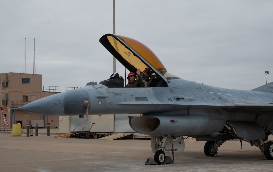 The pilot sits in an F-16 Fighter Jet and waves at the crowd.