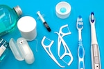 Different types of dental floss, toothbrushes, bottles, and a syringe on a light blue background