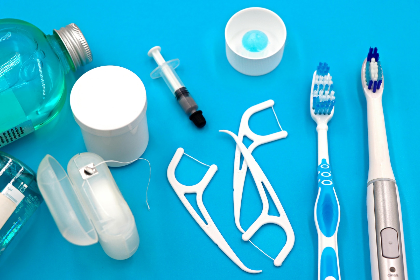 Different types of dental floss, toothbrushes, bottles, and a syringe on a light blue background