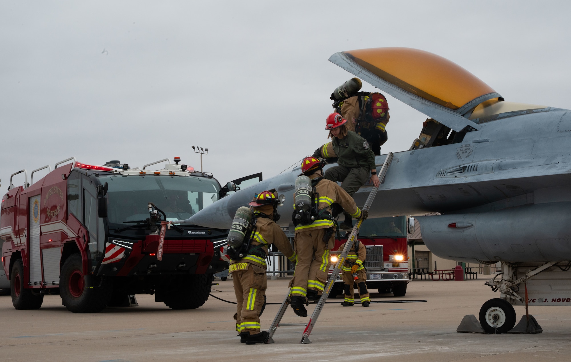 Three firefighters pull out a pilot from an F-16 fighter jet during a rescue demonstration.