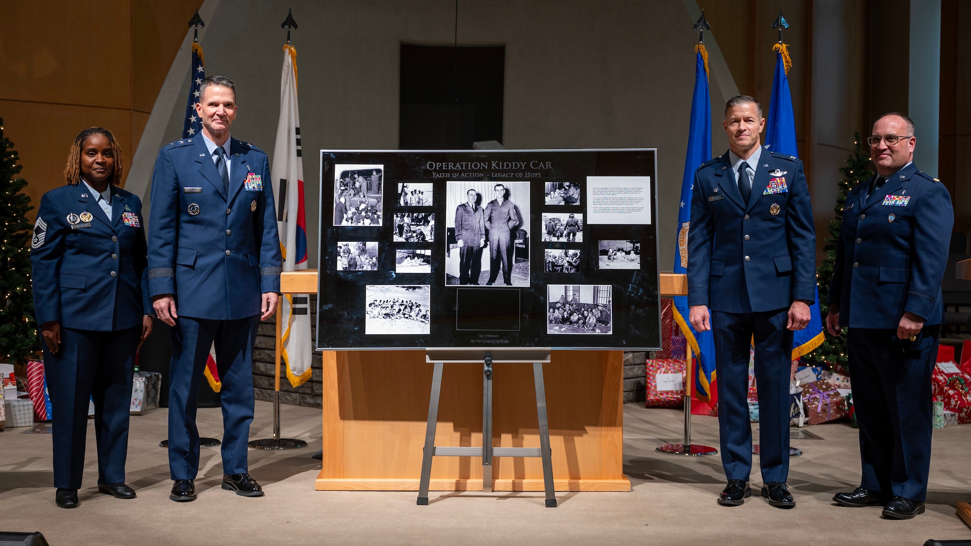 U.S. Air Force service members pose with the Operation Kiddy Car plaque during an anniversary ceremony at Osan Air Base, Republic of Korea, Dec. 17, 2025. Lt. Col. Russell Blaisdell, a chaplain, and Staff Sgt. Merle Strang commandeered several trucks at the port of Incheon, transporting more than 1,000 children to an air base in Gimpo, where they boarded 16 Douglas C-54 Skymasters and were evacuated to Jeju. The actions of Blaisdell and Strang exemplified courage, compassion, and decisive leadership in the face of crisis, showcasing the core mission of the Chaplain Corps by safeguarding innocent lives amid chaos and uncertainty. (U.S. Air Force photo by Staff Sgt. Sarah Williams)