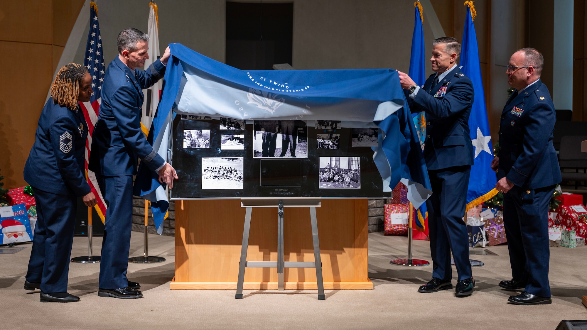U.S. Air Force Maj. Gen. Trent Davis, left center, Chief of Chaplains for the U.S. Air Force, and U.S. Air Force Col. Ryan Ley, right center, 51st Fighter Wing commander, unveil an Operation Kiddy Car plaque during an anniversary ceremony at Osan Air Base, Republic of Korea, Dec. 17, 2025. Lt. Col. Russell Blaisdell, a chaplain, and Staff Sgt. Merle Strang commandeered several trucks at the port of Incheon, transporting more than 1,000 children to an air base in Gimpo, where they boarded 16 Douglas C-54 Skymasters and were evacuated to Jeju. The actions of Blaisdell and Strang exemplified courage, compassion, and decisive leadership in the face of crisis, showcasing the core mission of the Chaplain Corps by safeguarding innocent lives amid chaos and uncertainty. (U.S. Air Force photo by Staff Sgt. Sarah Williams)