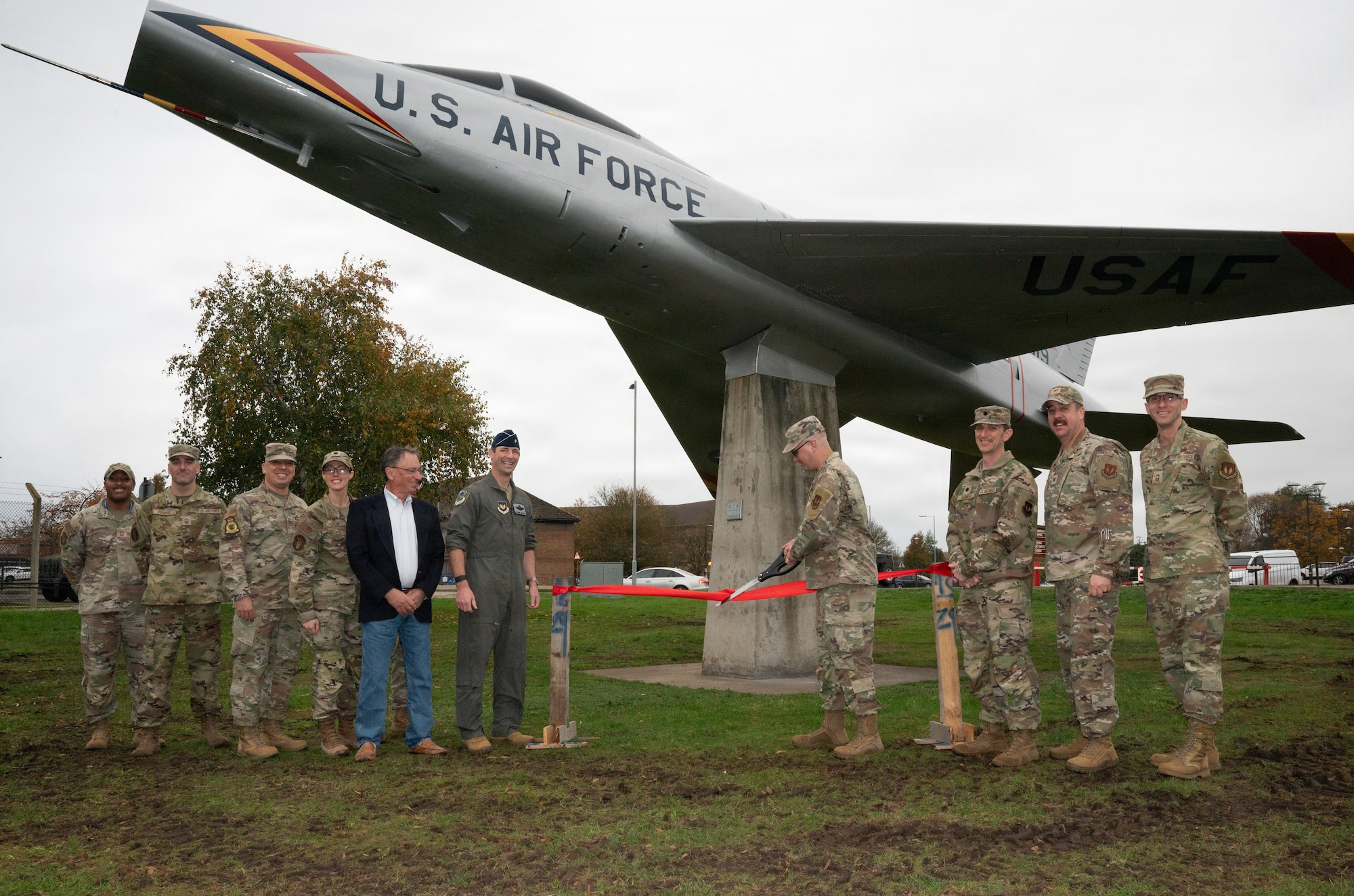 Military members cut a ribbon in front of a plane.