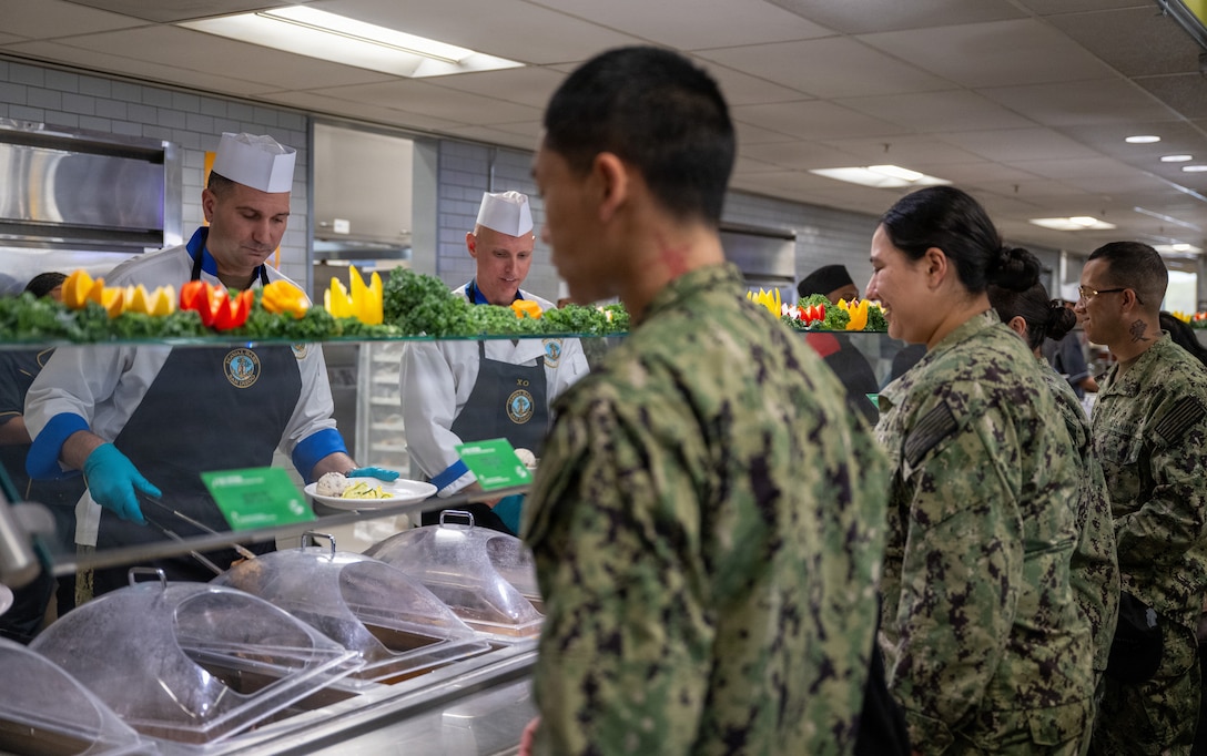 251211-N-CF730-1031 NAVAL BASE SAN DIEGO (Dec. 11, 2025) Cmdr. William R. Burkland, Executive Officer Naval Base San Diego, and Naval Base San Diego Command Master Chief Kristopher Freyberg serve various hot food items as part of the Christmas special meal at Naval Base San Diego, Dec. 11, 2025. Defense Logistics Agency Subsistence supply chain helps to keep morale high by giving servicemembers around the globe the smells and tastes of the December holidays.  (U.S. Navy photo by Interior Communications Electrician 2nd Class Ulrika Mendiola)