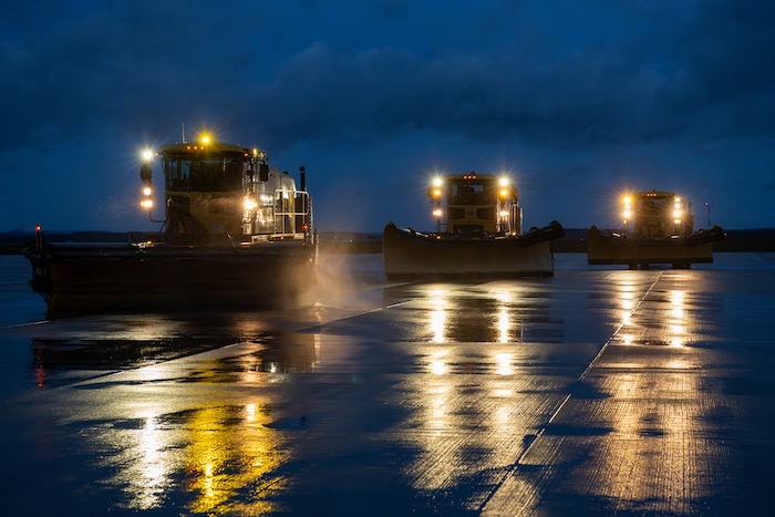 Snow removal vehicles drive on a road.