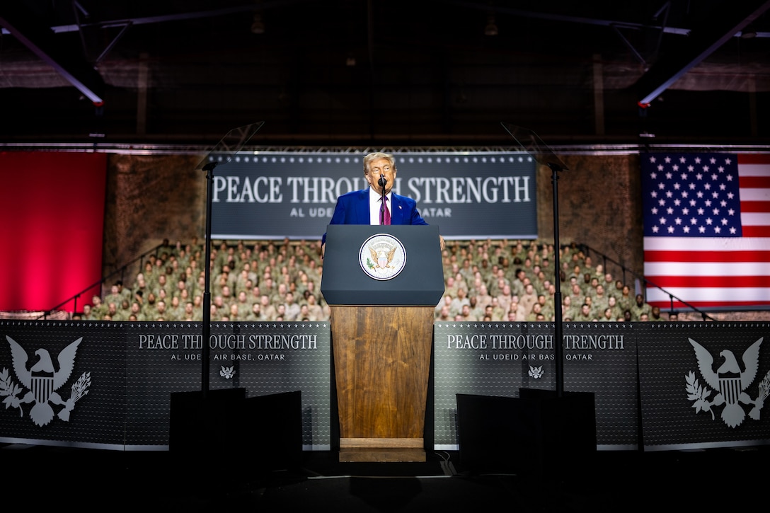 President Donald J. Trump speaks at a lectern with an audience of service members behind him.