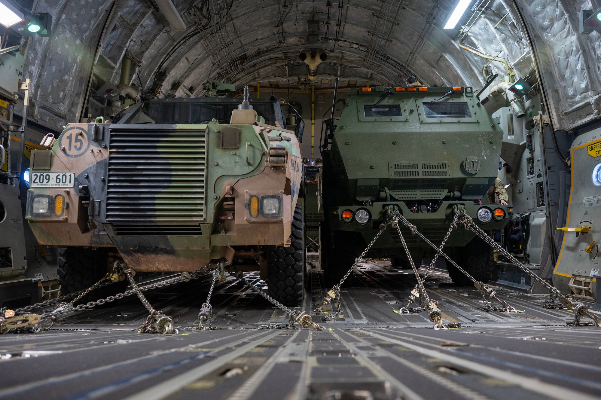 a shot of two military vehicles from the front taken in a military cargo plane with chains holding each vehicle in place