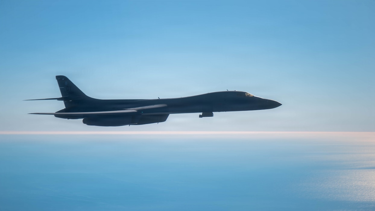 An aircraft flies with blues skies and water behind it
