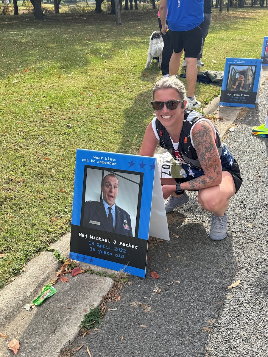Tech. Sgt. Kathryn Parker, 446th Airlift Wing public affairs specialist, poses for a photo by a picture of her deceased husband at the Marine Corps Marathon in Arlington, Virginia, on Oct. 26, 2025.