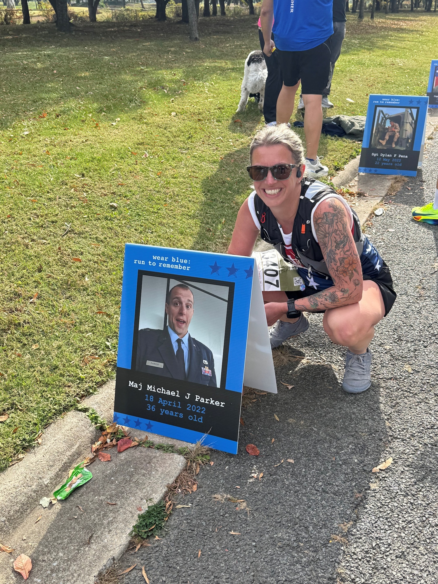 Tech. Sgt. Kathryn Parker, 446th Airlift Wing public affairs specialist, poses for a photo by a picture of her deceased husband at the Marine Corps Marathon in Arlington, Virginia, on Oct. 26, 2025.
