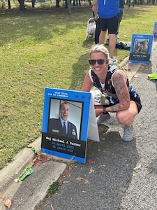 Tech. Sgt. Kathryn Parker, 446th Airlift Wing public affairs specialist, poses for a photo by a picture of her deceased husband at the Marine Corps Marathon in Arlington, Virginia, on Oct. 26, 2025.