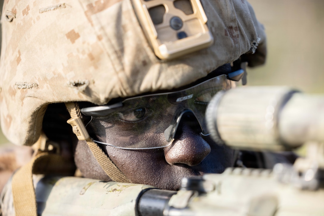 A close-up of a Marine wearing a helmet looking through the scope of a weapon.