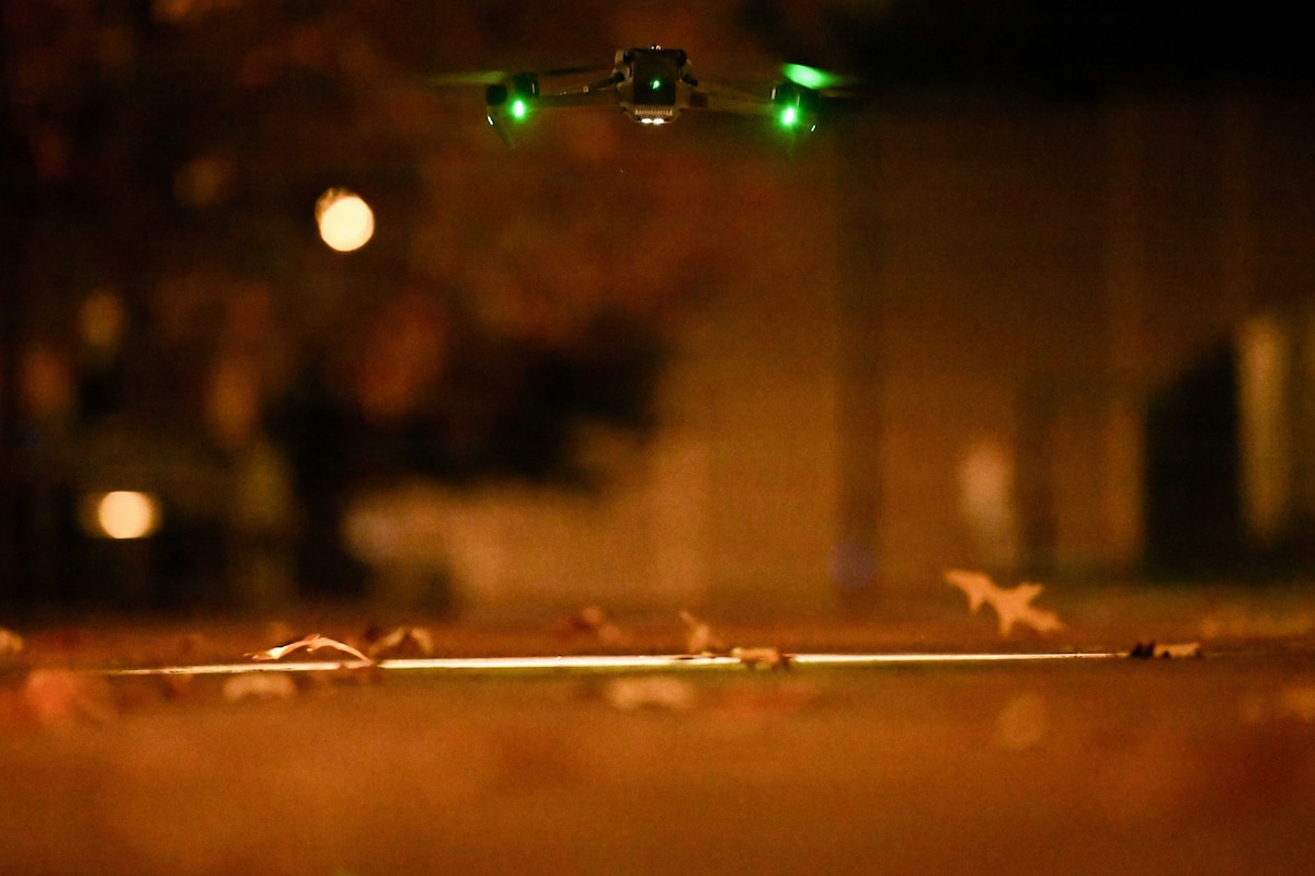A small drone launches from the ground outside at night.