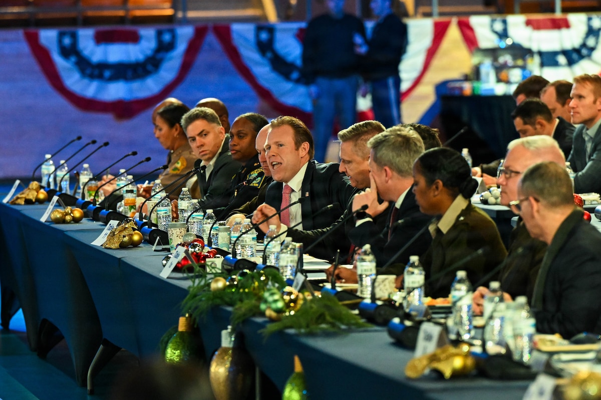 A man in business attire sits at a long table with people in similar attire.