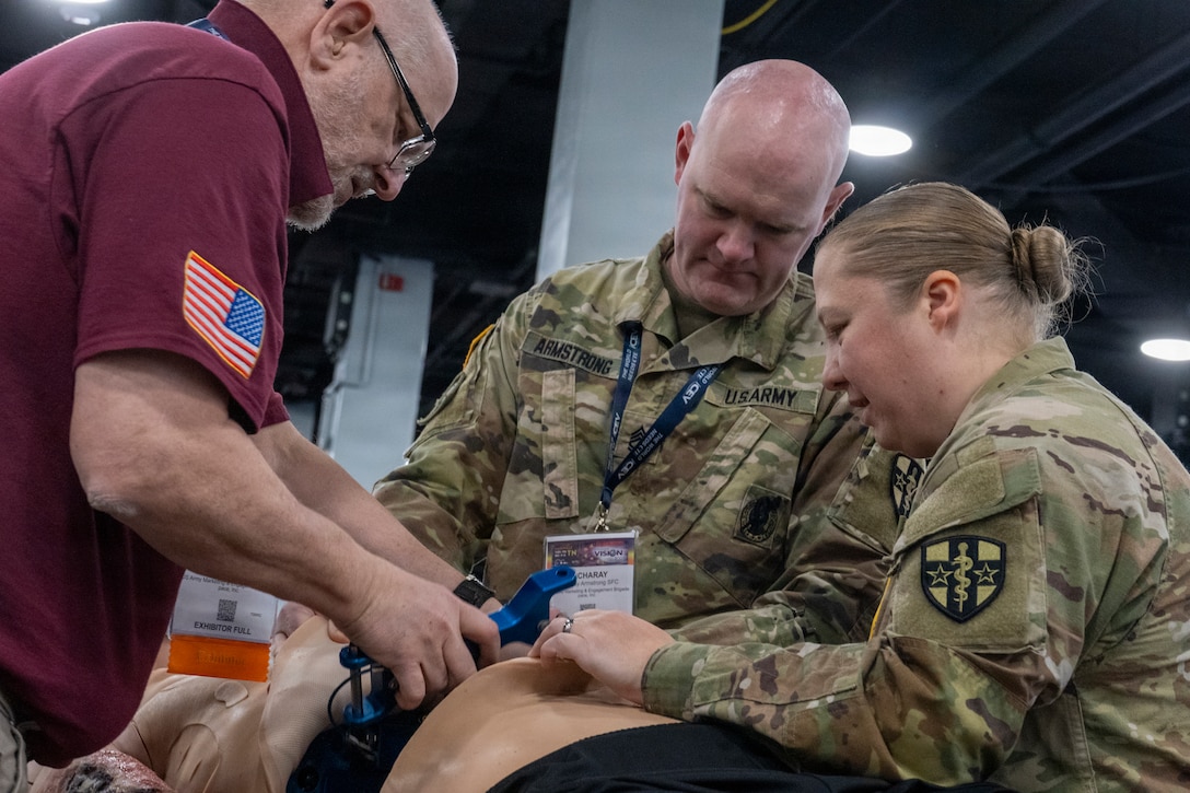 two soldiers wearing u.s. army uniforms demonstrate on a mannequin with a man wearing a polo shirt.