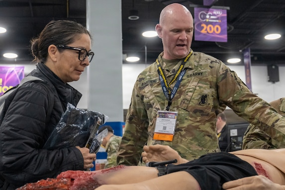 man wearing U.S. Army uniform talks to lady standing by a medical mannequin.