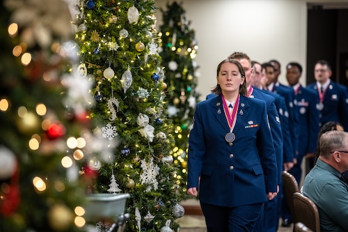A procession of women and men in formal Air Force dress uniforms alongside decorated holiday trees