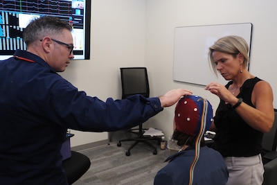 Public Health Service Lt. Austin D Hamilton, left, a licensed supervisory psychologist with the Fort Carson Intrepid Spirit Center, and Kirsten Larson, an ISC psychometrist, fine tune the connection on a neurofeedback Electro-Cap worn by Suzanne Martin, an ISC neuropsychologist, while testing out new equipment for use in treatment of traumatic brain injury and other diagnoses. Neurofeedback is an evidenced-based practice that allows clinicians to “map” brain activity levels and compare the results to what is considered normal brain activity.